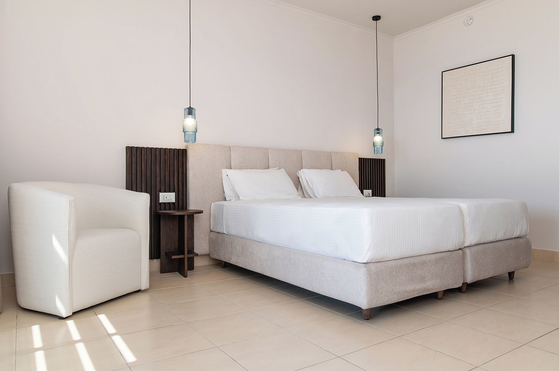 Quarto moderno com cama, mesas de cabeceira, uma cadeira e luminária fixa na parede.