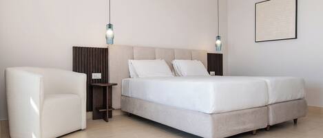 Quarto moderno com cama, mesas de cabeceira, uma cadeira e luminária fixa na parede.