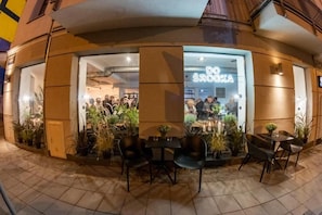 An outdoor seating area with tables and chairs, a storefront with the name 'DO SROOKA' visible, and potted plants around the seating. - Hotel Śródka (Poznan)