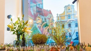 A table with various food items and decorative plants in front of a window with a view of buildings. - Hotel Śródka (Poznan)