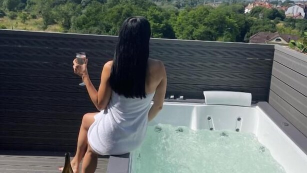 A woman sitting by a hot tub with a view of a cityscape. - Hotel Śródka (Poznan)