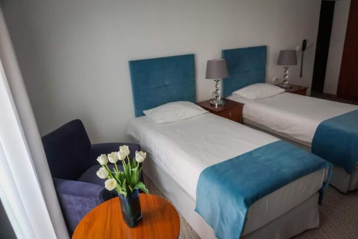 A hotel room with two beds, a small table with a vase of flowers, and a chair.