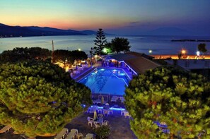 A pool area with lounge chairs and umbrellas, surrounded by trees, overlooking a body of water and distant mountains. - Valais Hotel (Zakynthos)