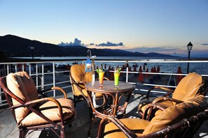 A terrace with wicker chairs and a table, overlooking a body of water and mountains. - Valais Hotel (Zakynthos)