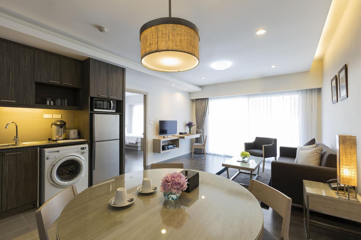 Een moderne hotelkamer met keuken, eethoek en zithoek. Er is een wasmachine, een eettafel met stoelen, een bank en een televisie.