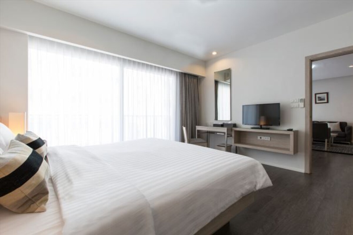 A modern hotel room with a large bed, a desk with a flat-screen TV, and a walk-in closet.