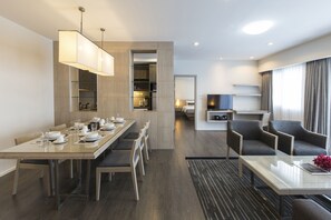 A modern hotel room with a dining area, a living area with a TV, and a separate kitchen.