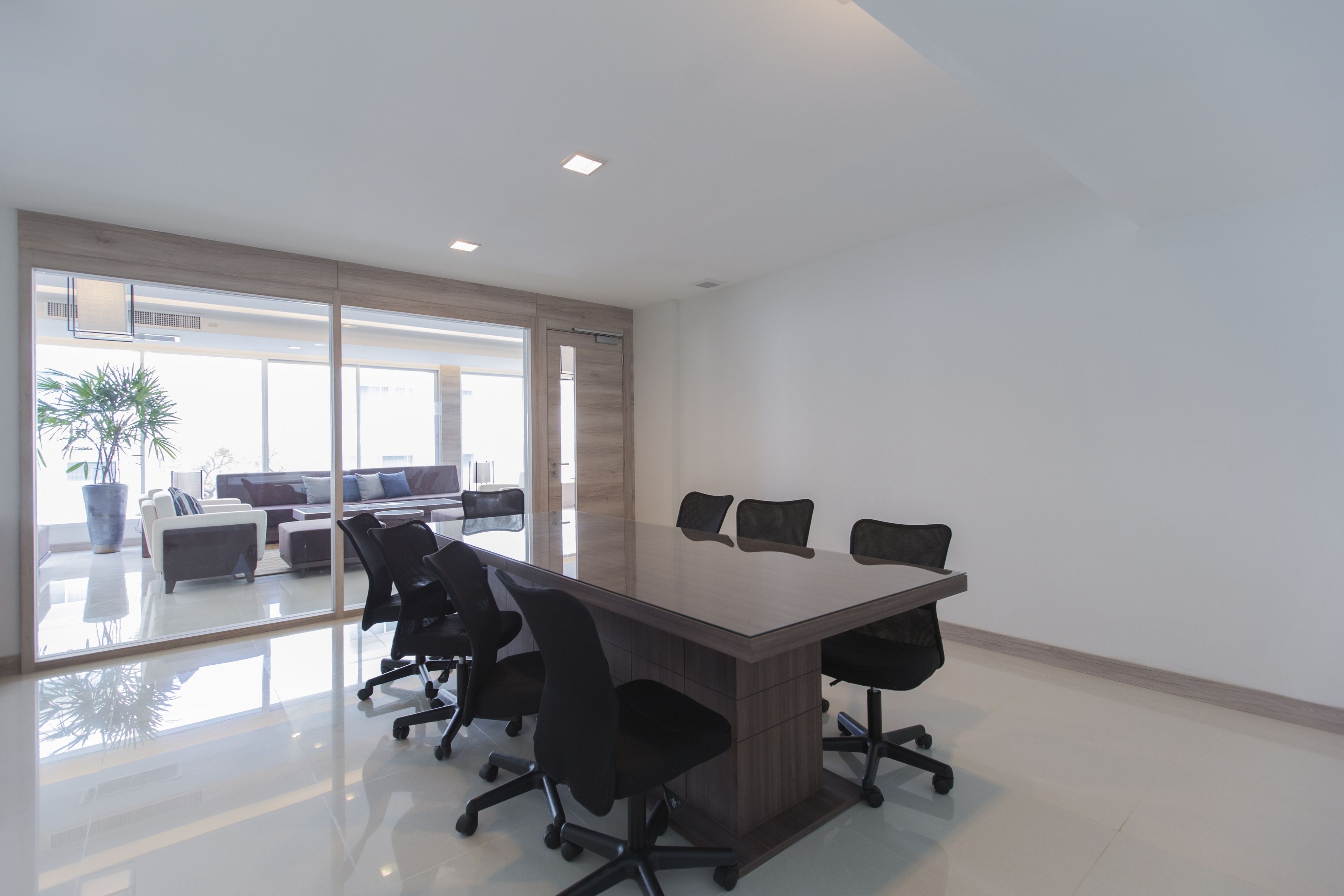 A modern conference room with a large rectangular table, black office chairs, and a glass partition.