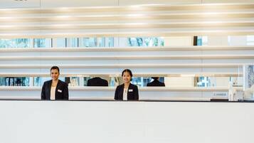 A reception area with two staff members standing behind a counter, a name tag on the counter, and a sign that reads "CASHIER".