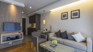 A modern living room with a flat-screen TV, a grey sofa, a coffee table, and a dining area in the background.
