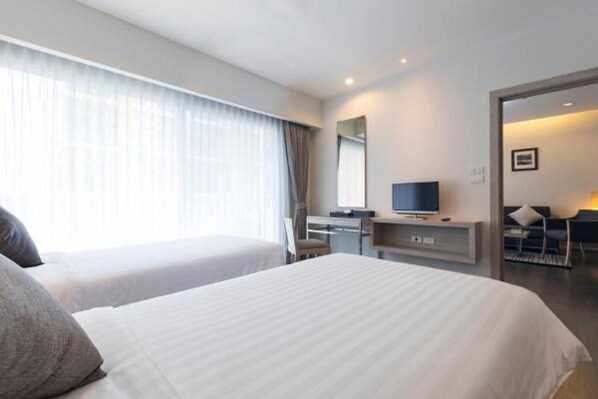 A hotel room with two beds, a desk, a TV, and a view of the outside.