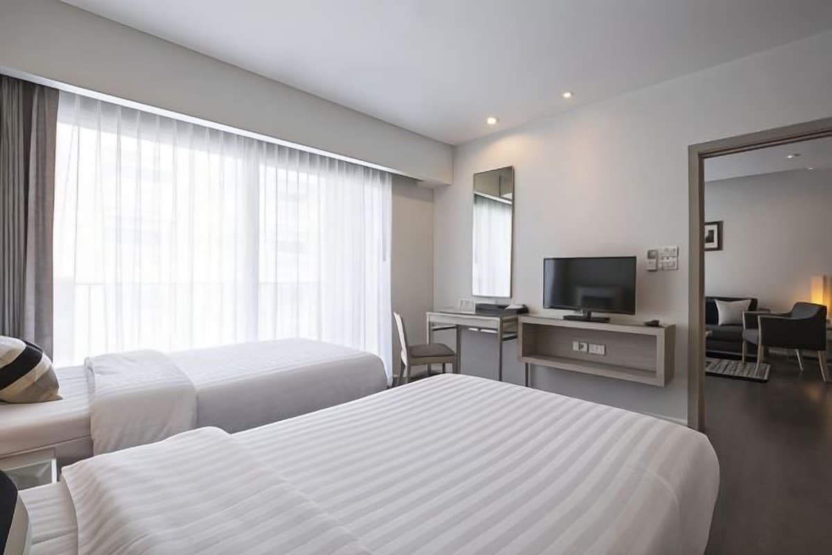 Habitación de hotel con dos camas, un escritorio con televisor y un ventanal con cortinas.