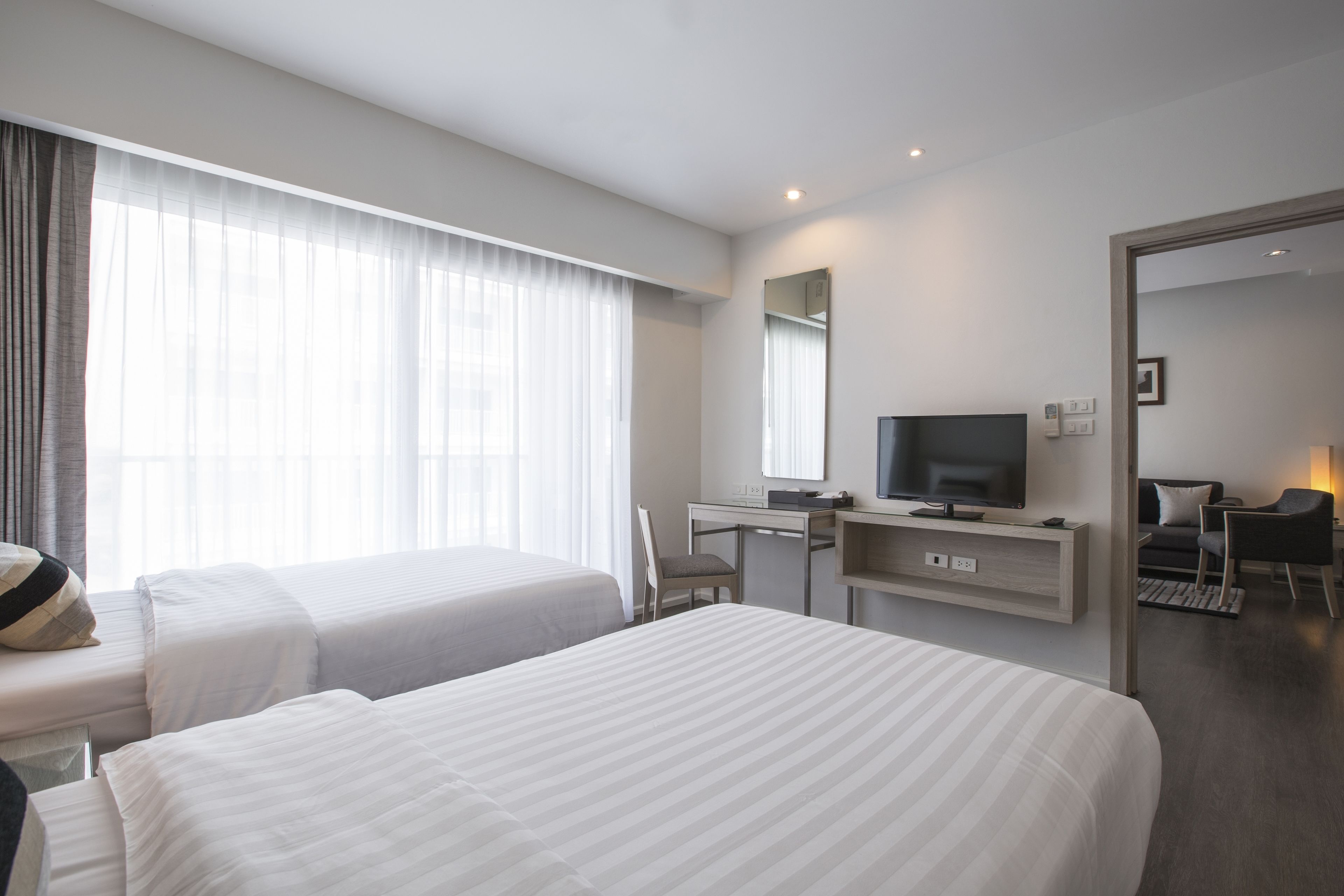 A hotel room with two beds, a desk with a TV, a mirror, and a view of the outdoors.