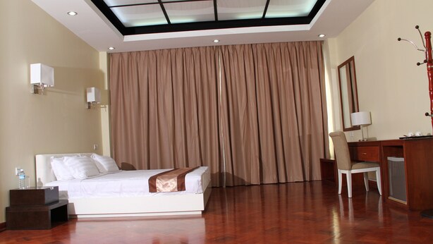 Habitación de hotel con cama, escritorio, silla y una ventana grande con cortinas.