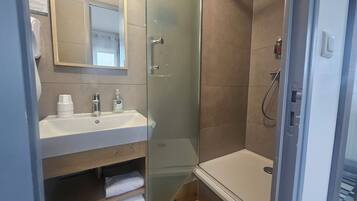 Une salle de bain moderne avec une douche à parois de verre, un lavabo avec un miroir et des articles de toilette.
