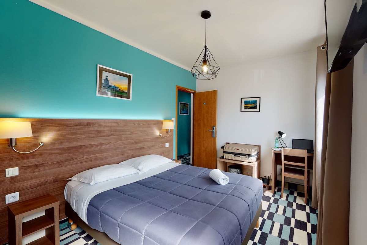 Hotellihuone, jossa on sänky, työpöytä, tuoli, lamppu ja taulu seinällä.