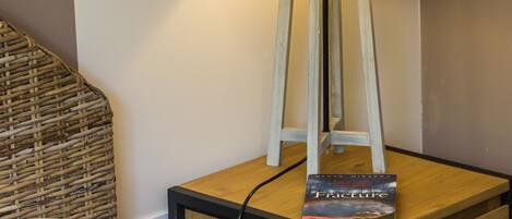 A bedside table with a lamp, a book titled "Fracture," and a power outlet.