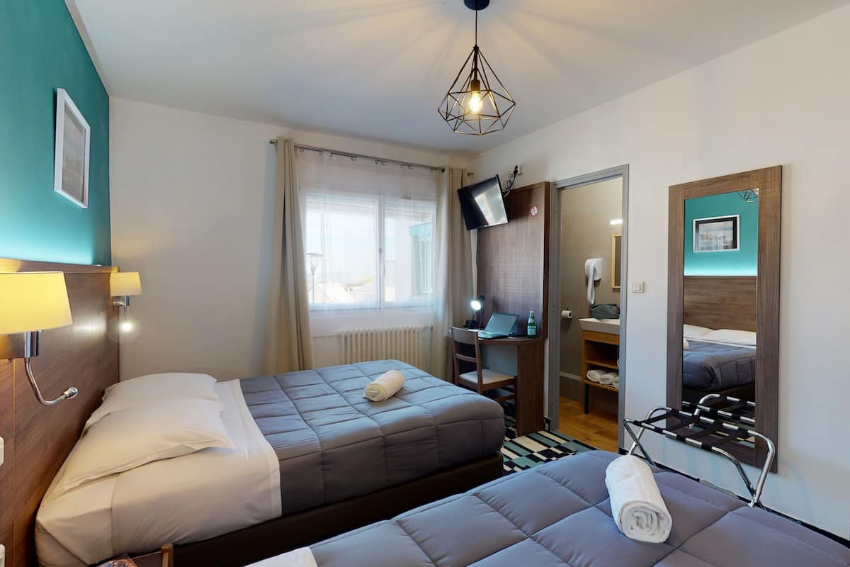Hotellihuone, jossa on kaksi sänkyä, työpöytä kannettavalla tietokoneella, televisio ja peili.