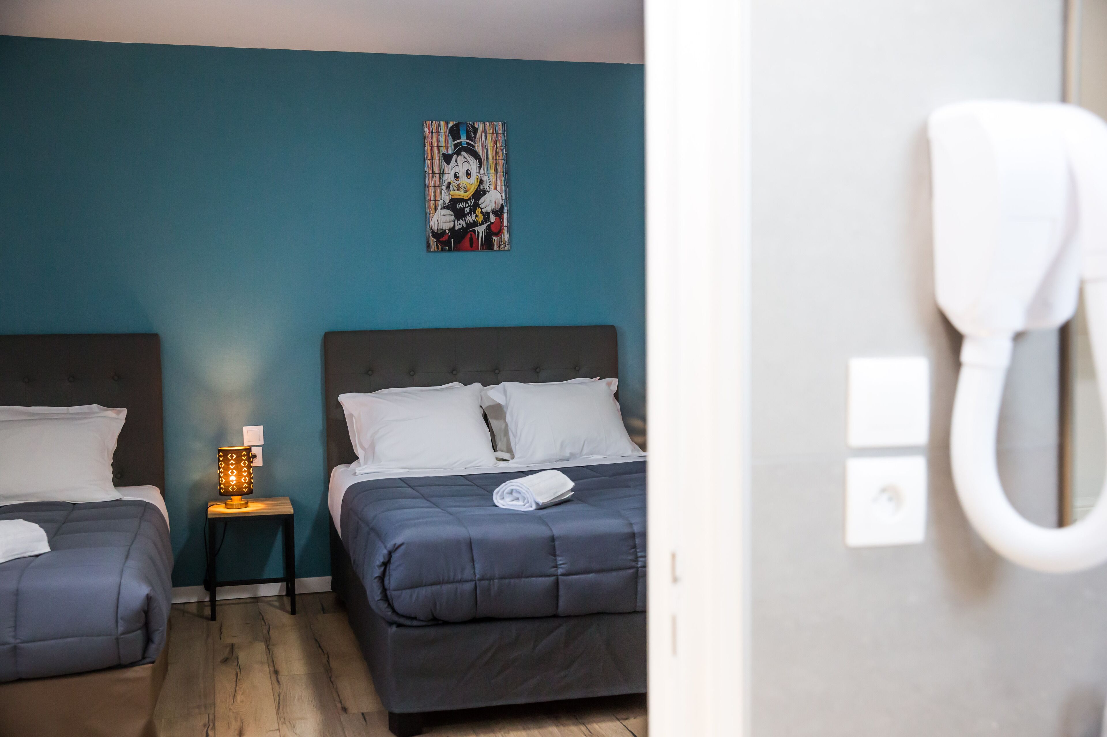 Habitación de hotel con dos camas, una mesita de noche con lámpara y un teléfono en la pared.