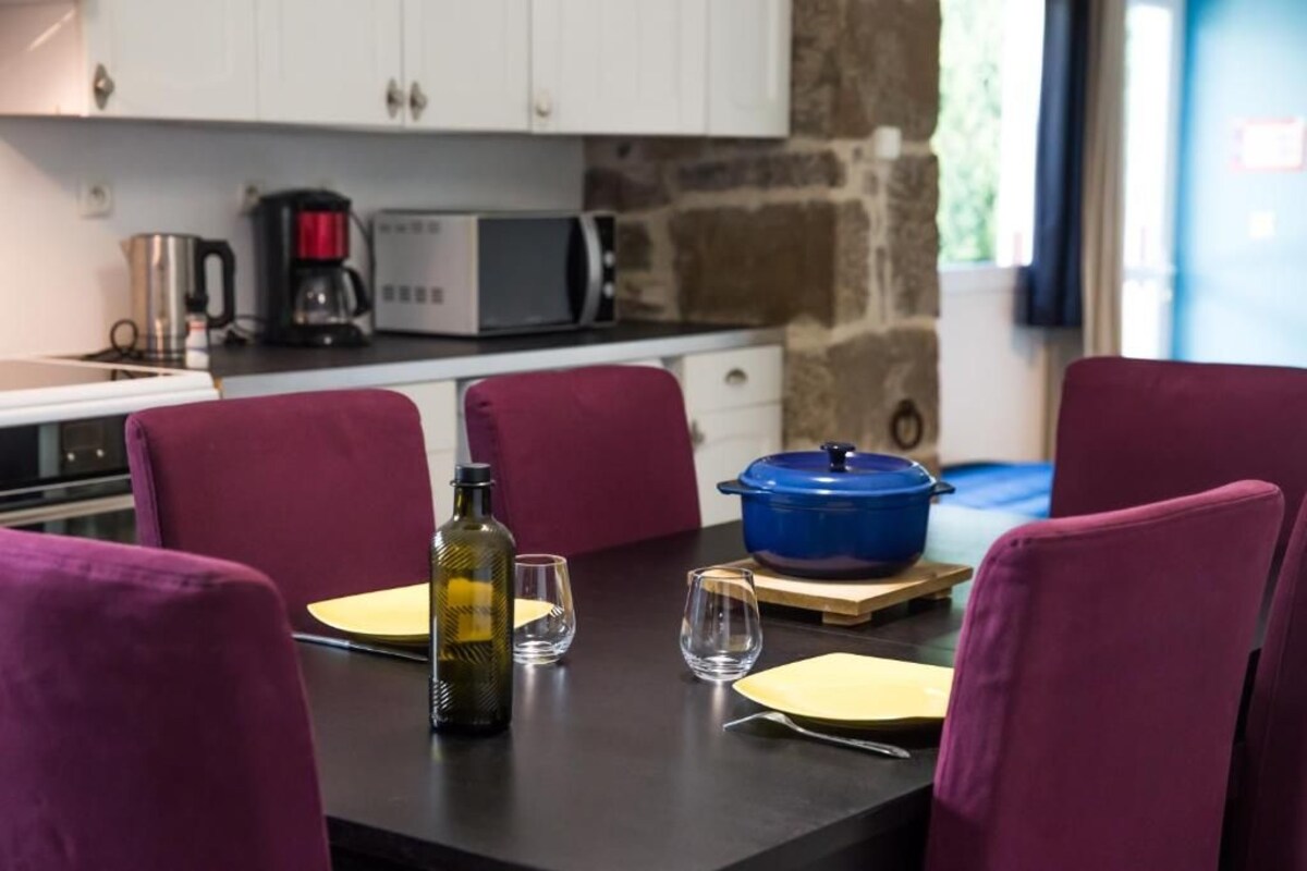 Una mesa de comedor con sillas moradas, una olla azul y una botella de aceite de oliva.
