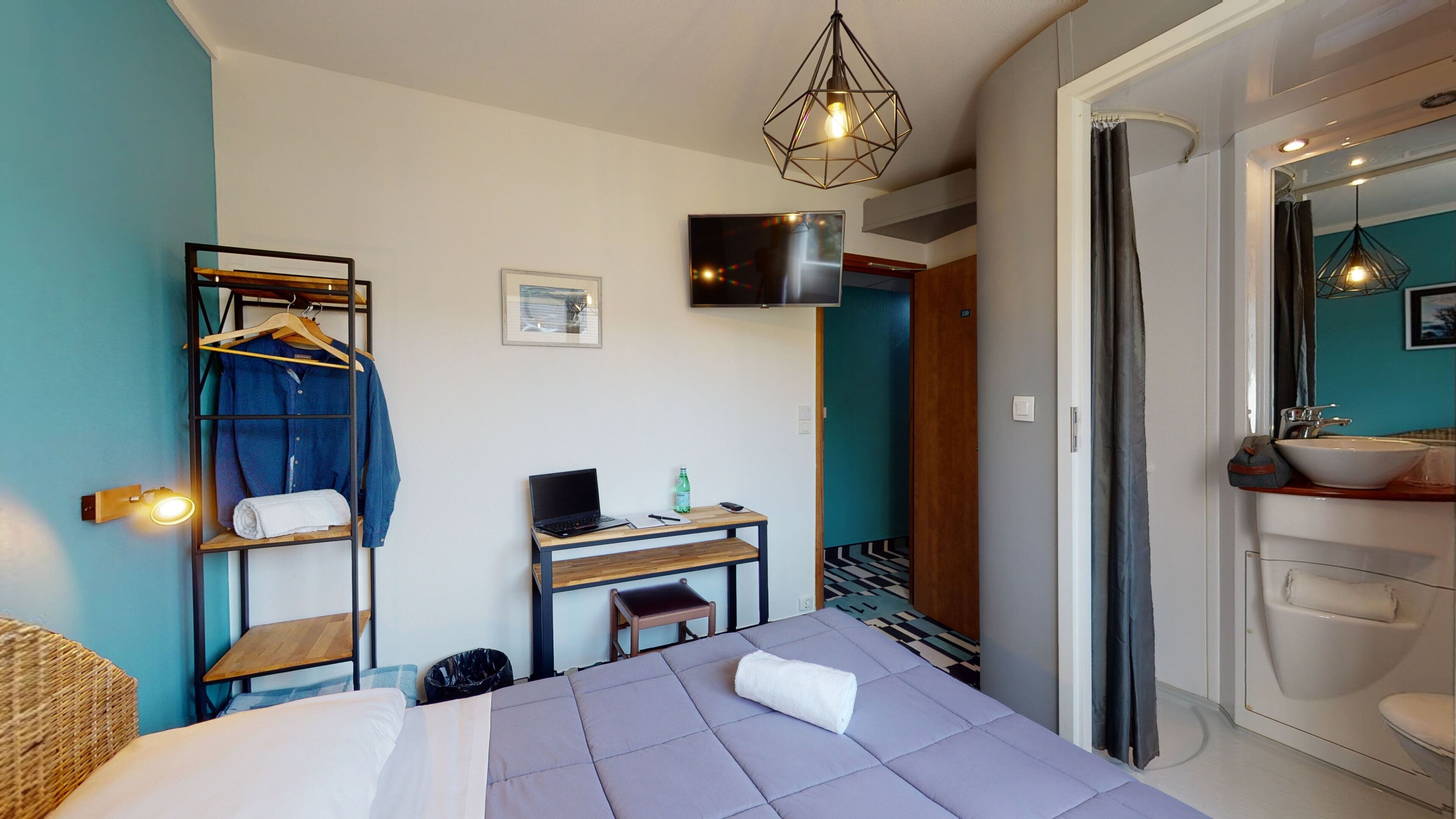 Una camera d'albergo con un letto, una scrivania con un portatile, una televisione, un armadio e un bagno.