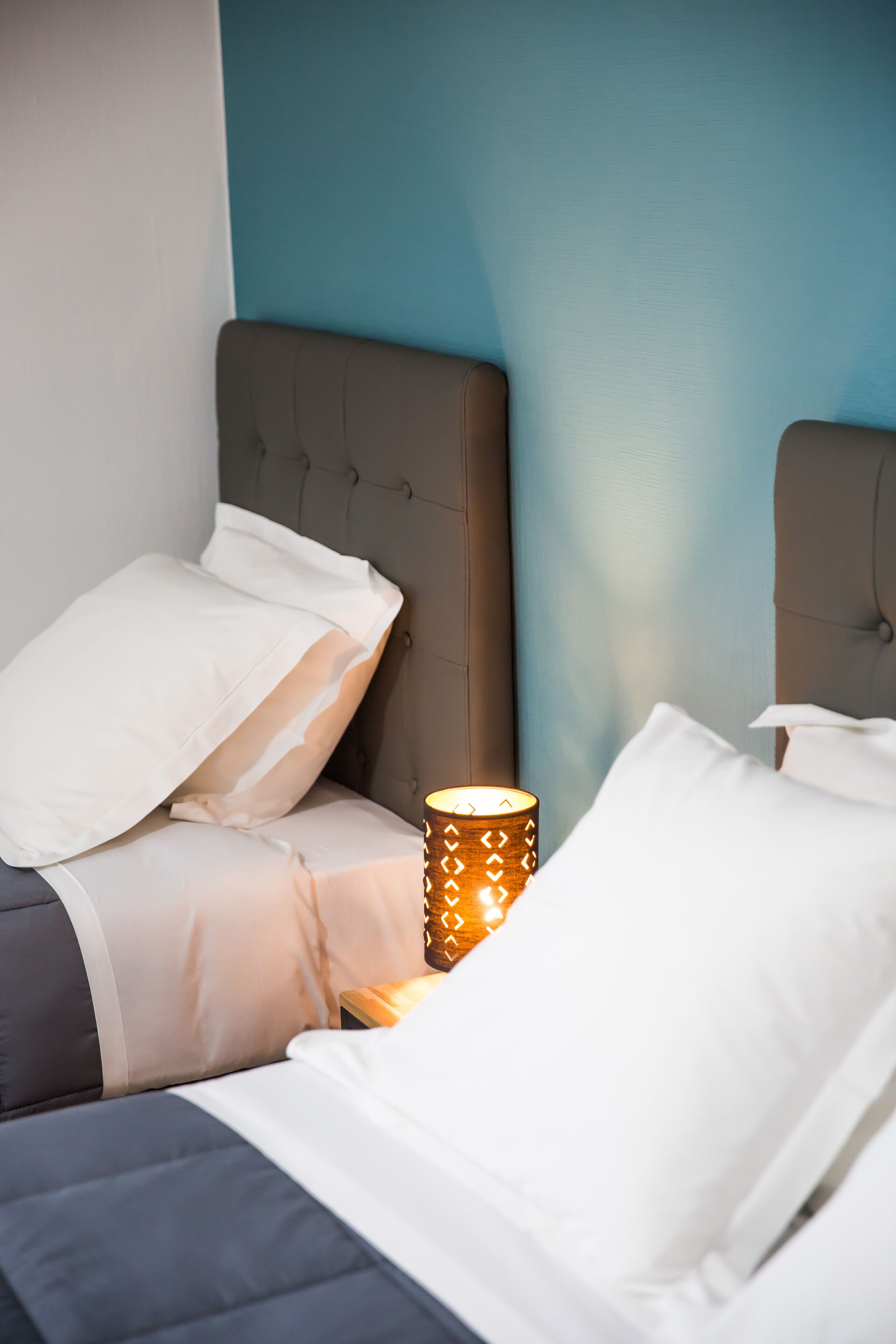 A neatly made bed with white and gray bedding, a bedside lamp, and a blue wall in the background.