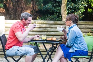 Two people seated at a table with food and drinks, outdoors with a wooden fence and greenery in the background. - Hôtel les Pieux (Les Pieux)