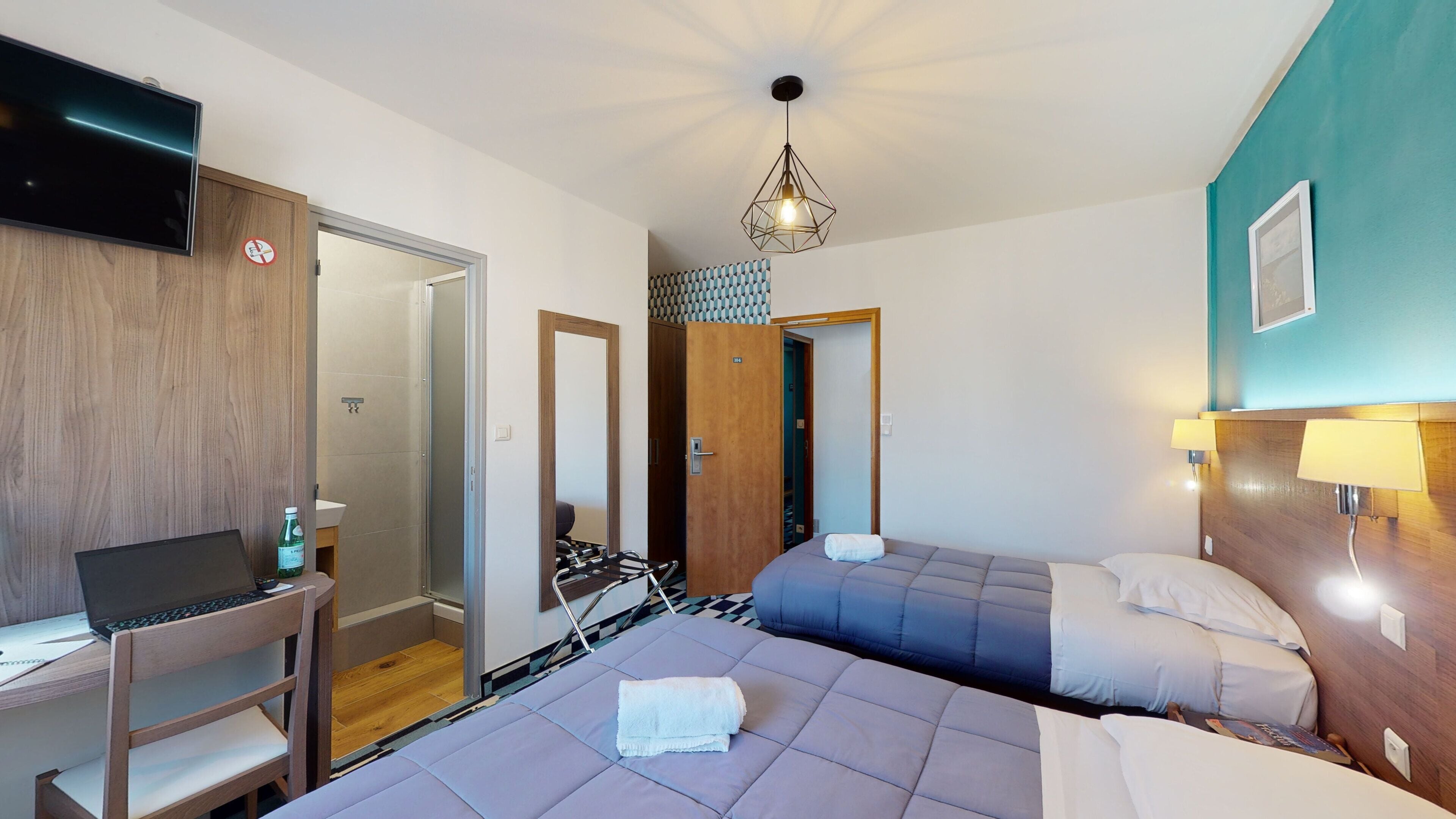 A hotel room with a bed, a desk with a laptop, a shower, and a TV.