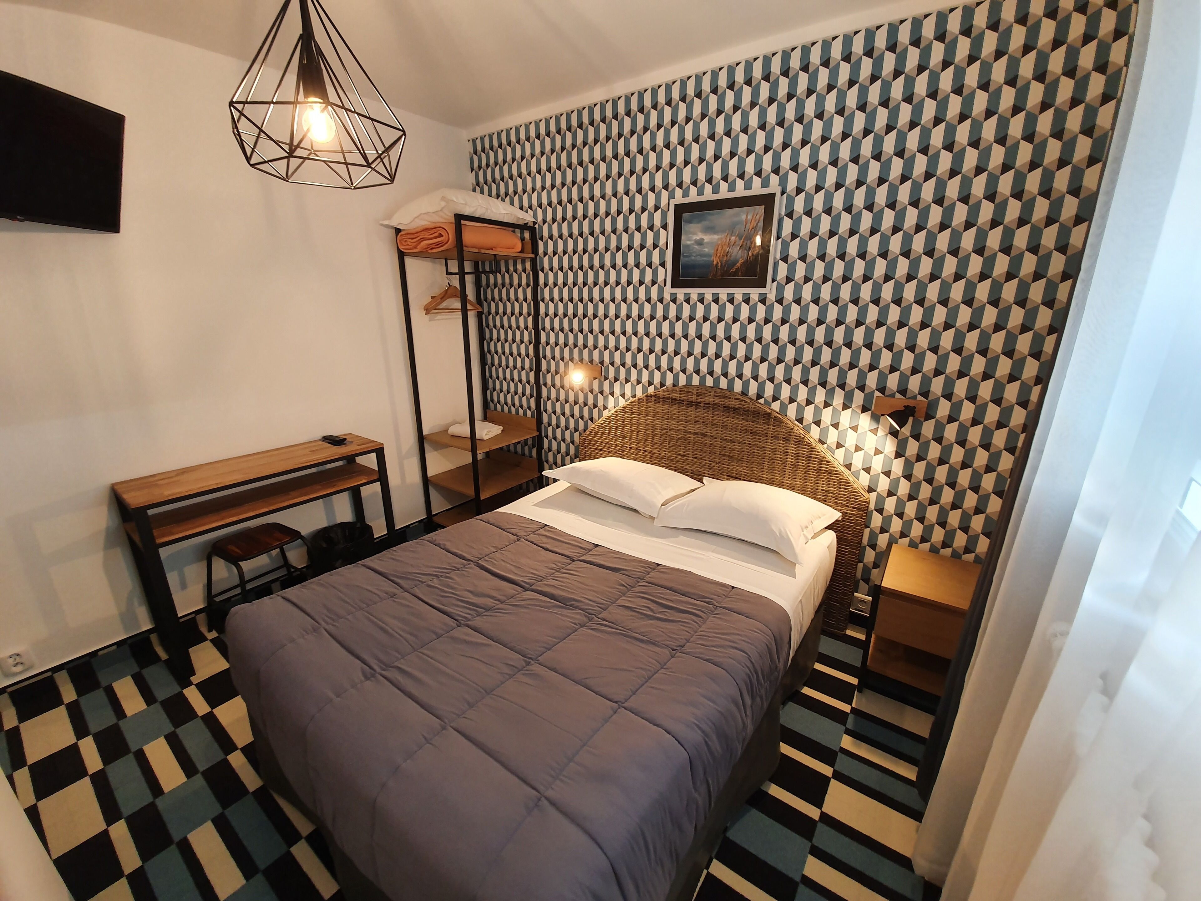 A modern bedroom with a bed, a desk, and a hanging light fixture.