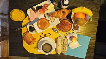 A breakfast tray with pancakes, ham, eggs, and fruits on a wooden table.