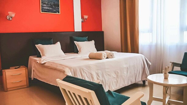 Een hotelkamer met een bed, nachtkastjes, een stoel, een klein rond tafeltje en een raam met gordijnen.