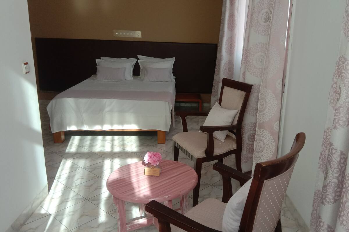 Een hotelkamer met een bed, een stoel, een klein tafeltje en een raam met gordijnen.