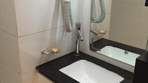 Een badkamer met een witte wastafel, een zwart aanrechtblad en een spiegel erboven. Een haardroger en een handdoekhouder zitten aan de muur.