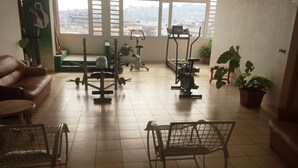 Een sportschool met trainingsapparatuur, een loopband en een stadszicht door grote ramen.