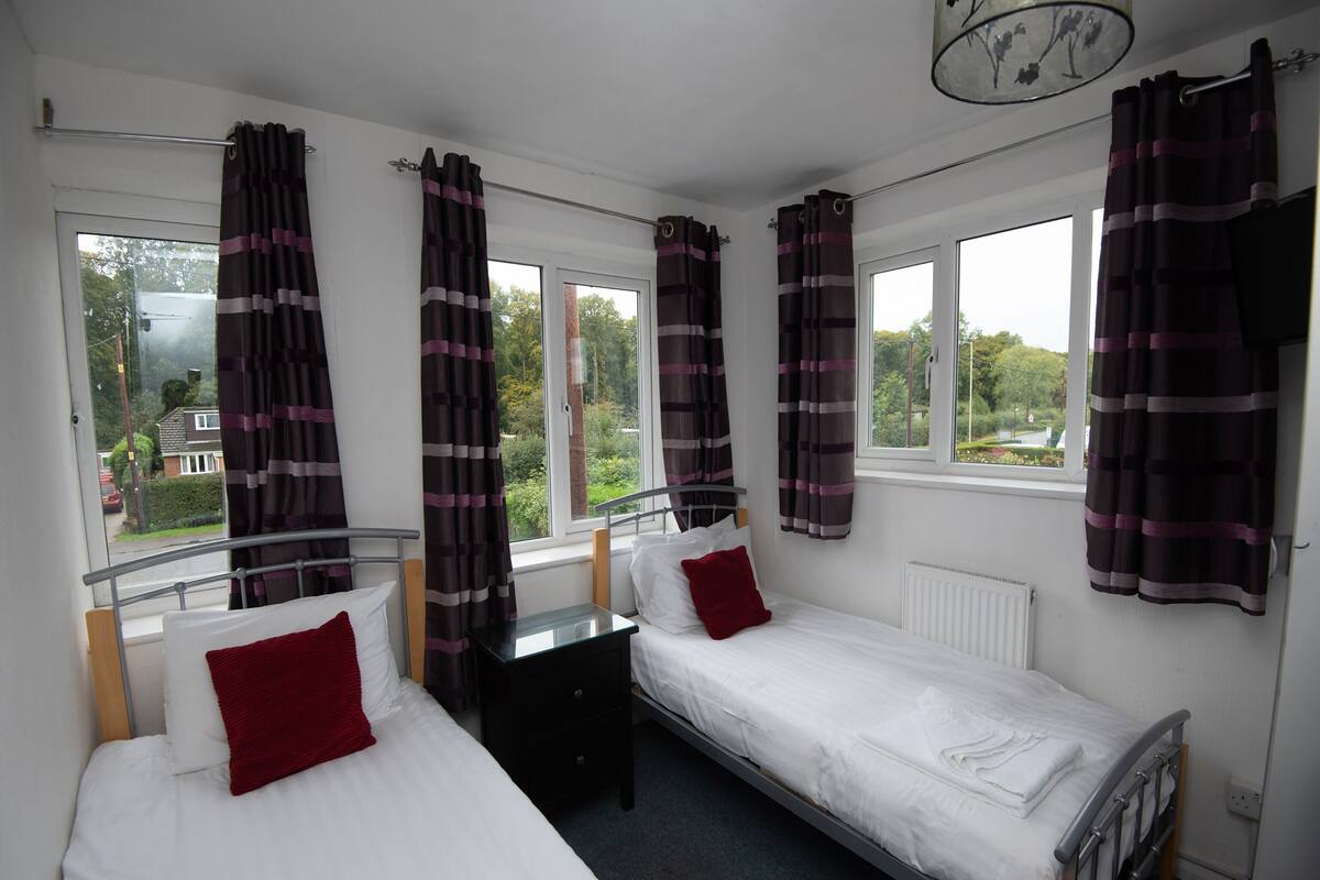 A room with two single beds, a small table, and a window with curtains.