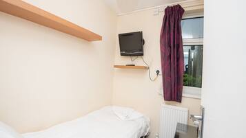 A small, clean room with a single bed, a mounted TV, a window with curtains, and a radiator.