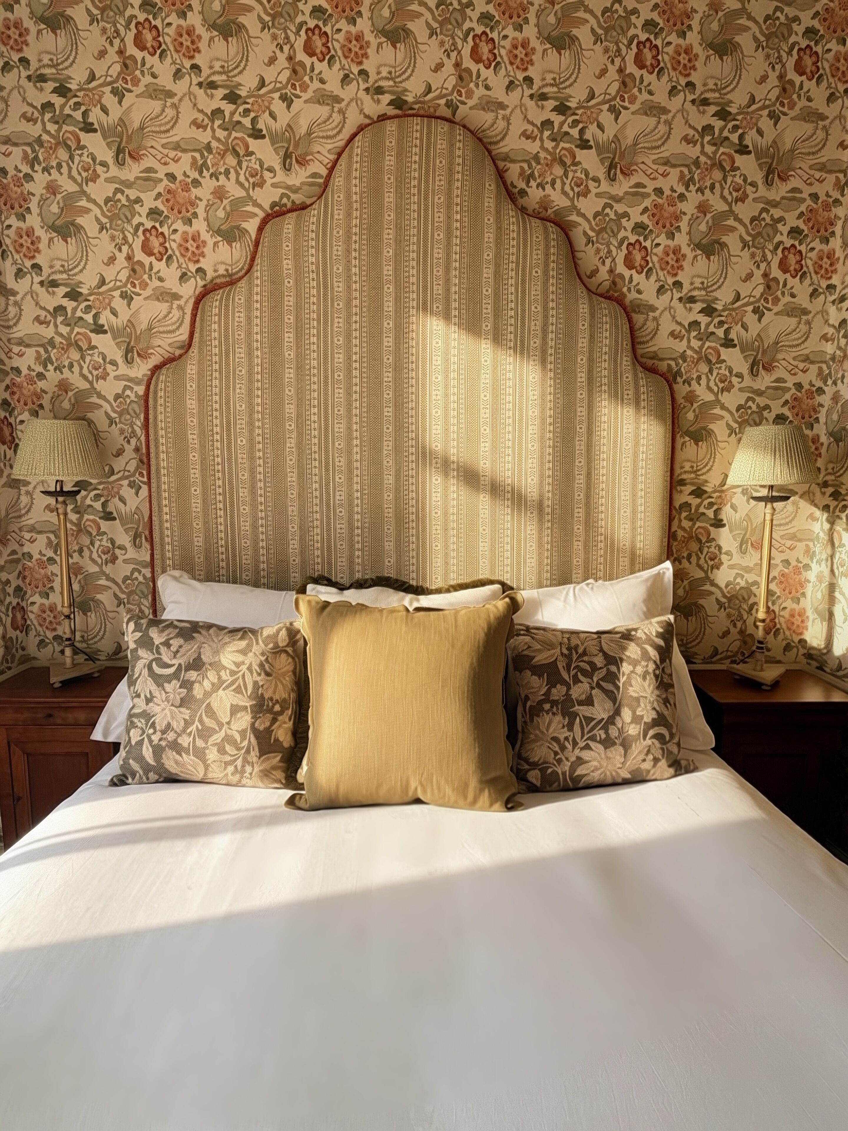 A bed with a striped headboard, floral-patterned pillows, and a nightstand with a lamp.
