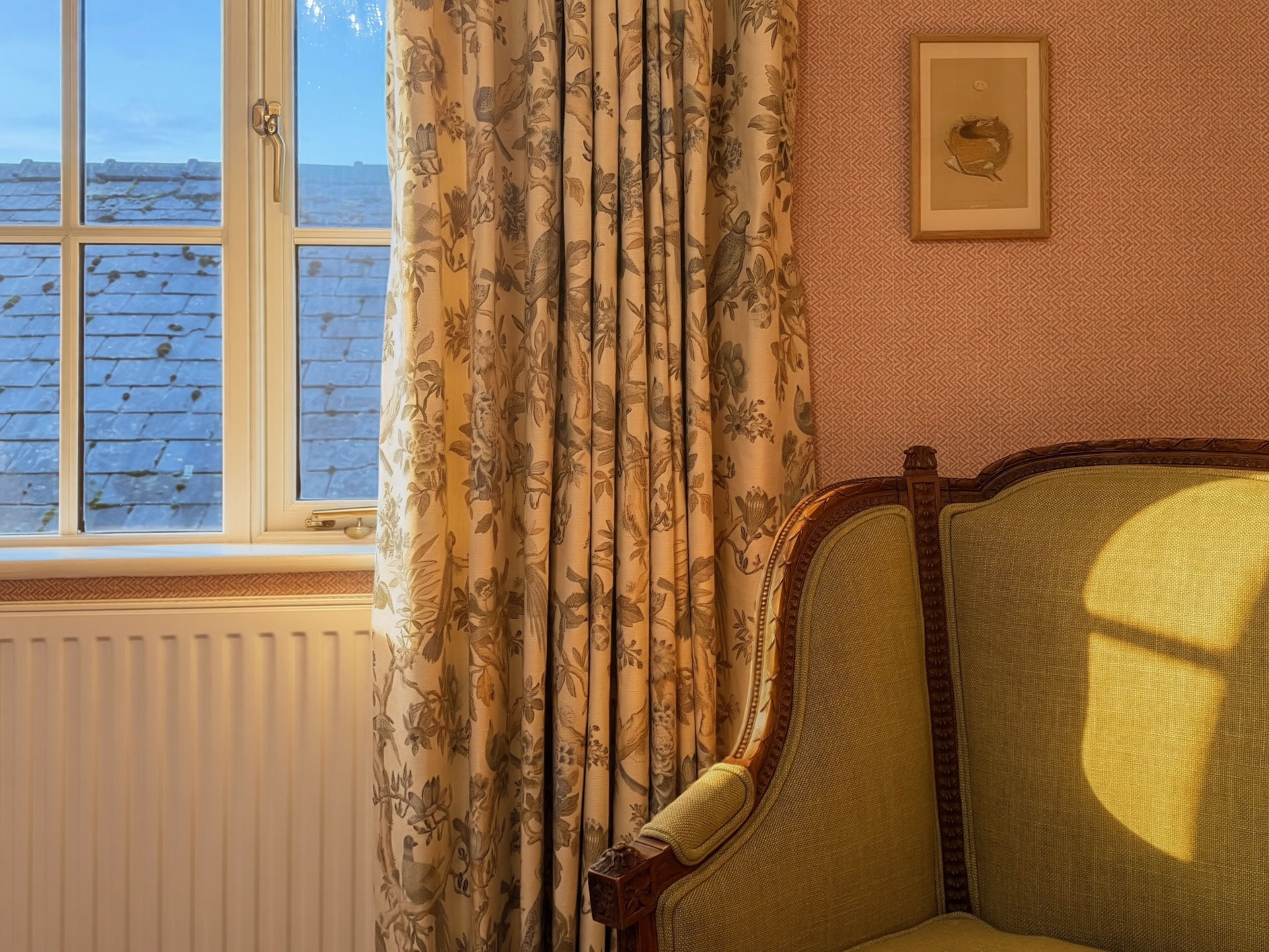 A room with a window, a radiator, a chair, and a framed picture on the wall.