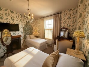 Une chambre d’hôtel avec deux lits, un lustre, un miroir, une lampe et un papier peint à motifs.