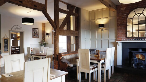 A rustic interior with exposed wooden beams, a fireplace, and a dining area with white furniture. - The Salwey Arms (Ludlow)