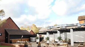 A patio area with picnic tables, a brick building, and a covered outdoor space. - The Salwey Arms (Ludlow)
