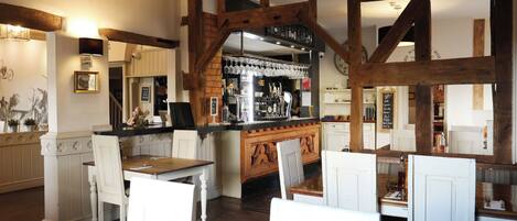 A restaurant with wooden beams, white chairs, a bar area, and a clock on the wall.