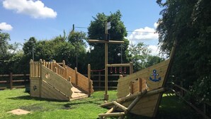 A playground with wooden structures, including a slide and climbing area, surrounded by grass and trees. - The Salwey Arms (Ludlow)