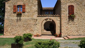 Un bâtiment en pierre doté d’une arche centrale, de volets en bois et de jardinières.