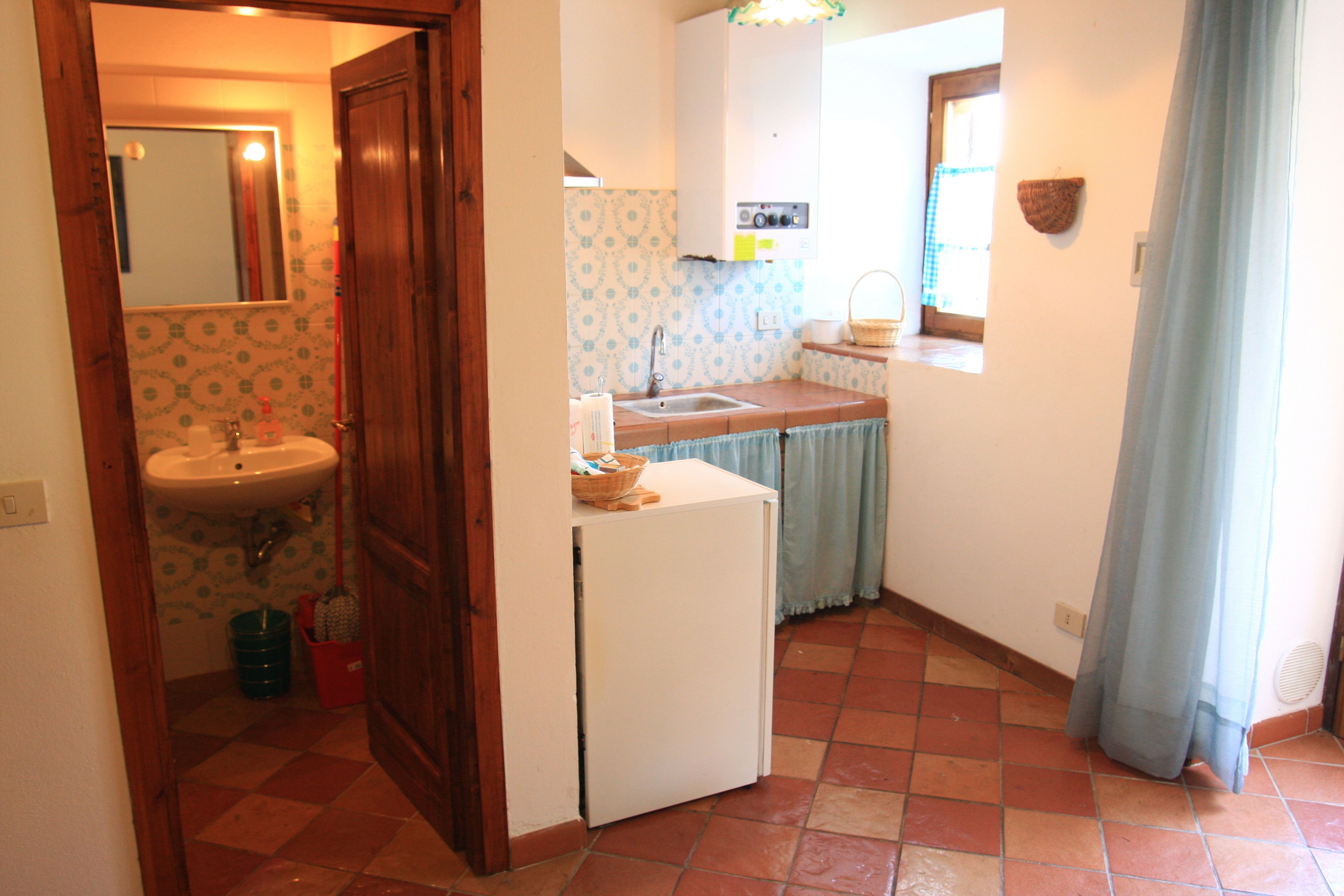 A compact kitchen with a sink, a small refrigerator, and a window with a curtain.