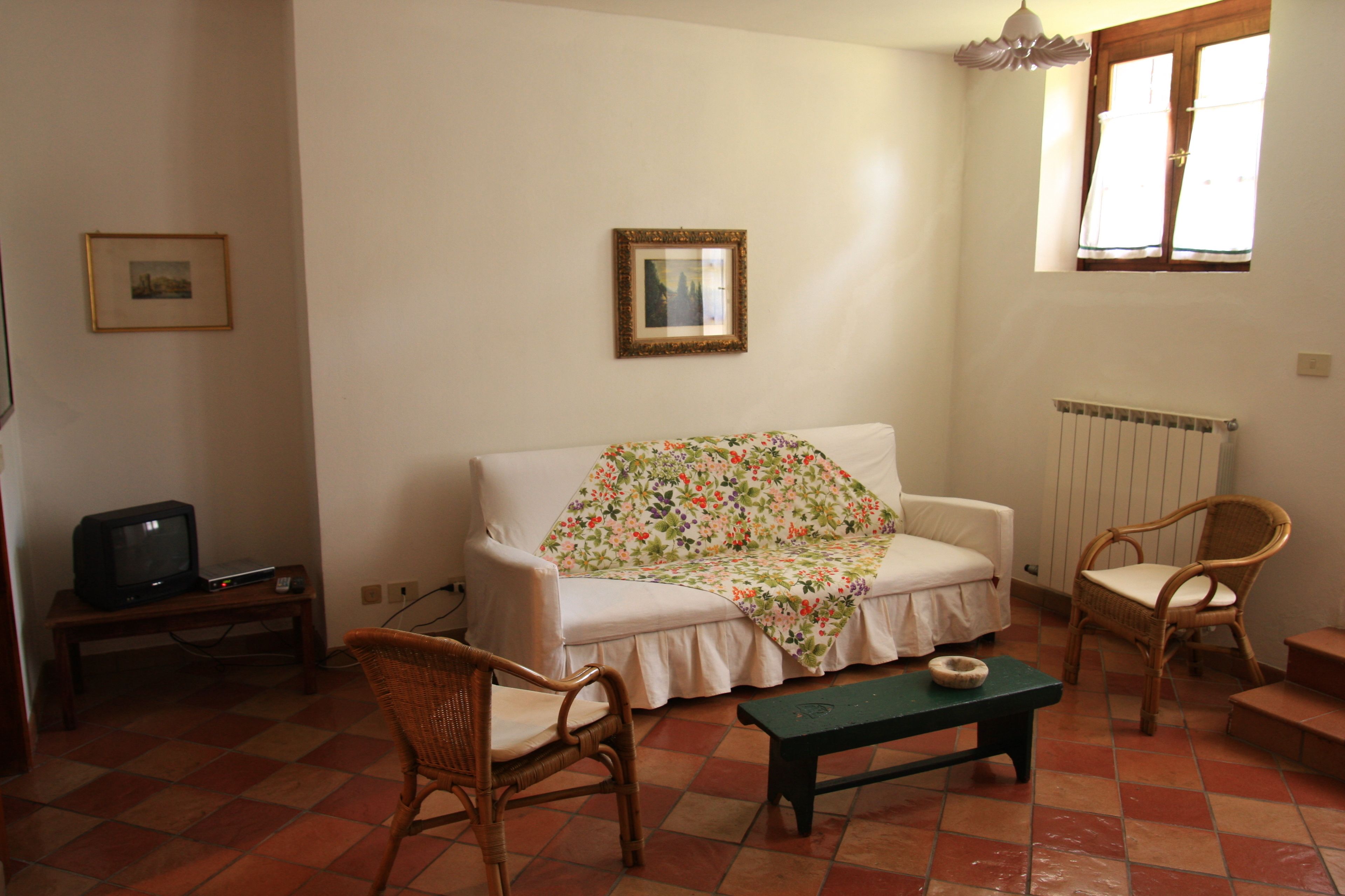 A living room with a sofa, two wicker chairs, a small table, a television on a stand, and a window with curtains.