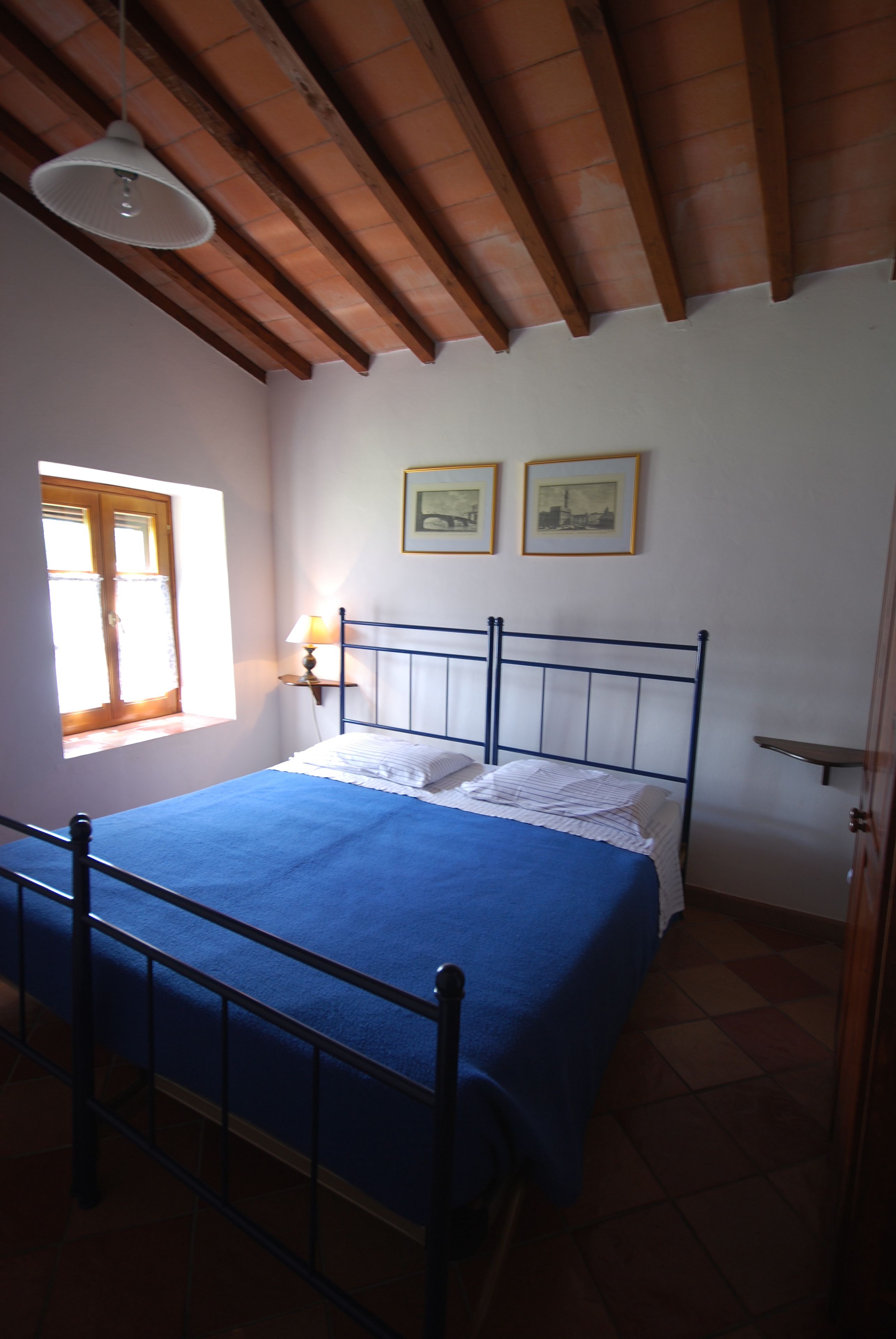 Ein Schlafzimmer mit einem Bett, einem Fenster, einer Lampe und zwei gerahmten Bildern an der Wand.