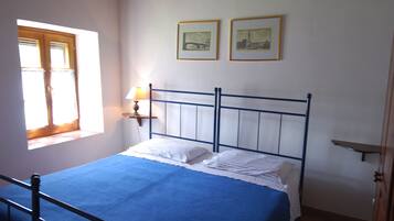 Ein Schlafzimmer mit einem Bett, einem Fenster, einer Lampe und zwei gerahmten Bildern an der Wand.