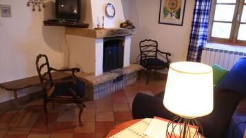 A living room with a fireplace, two wooden chairs, a television on a shelf, and a lamp on a table.