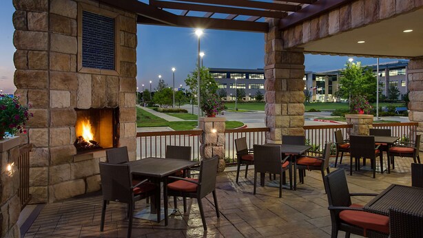 An outdoor patio with stone walls, a fire feature, and outdoor seating. - Hyatt Place DFW (Dallas)